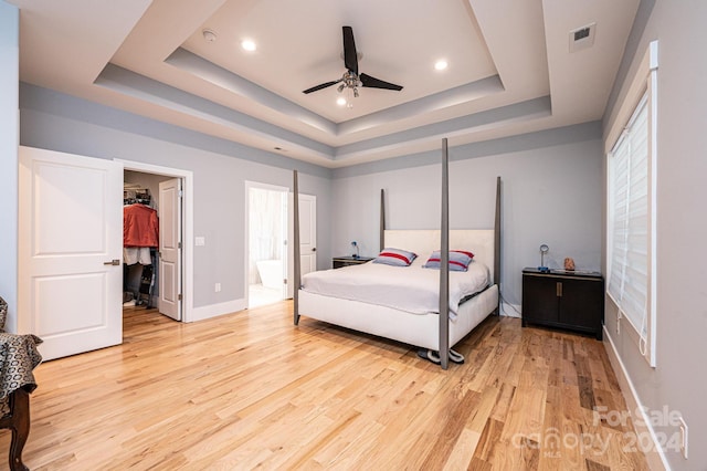 bedroom featuring ceiling fan, light wood-type flooring, and a tray ceiling