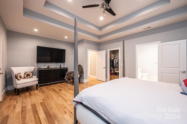 bedroom with light hardwood / wood-style flooring, a spacious closet, ceiling fan, and a tray ceiling