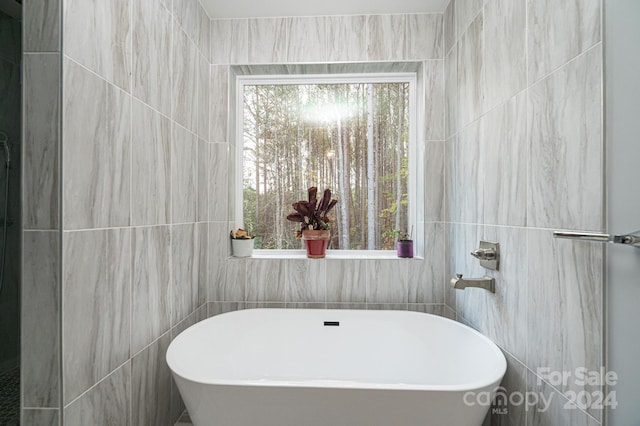 bathroom featuring plenty of natural light, a bath, and tile walls