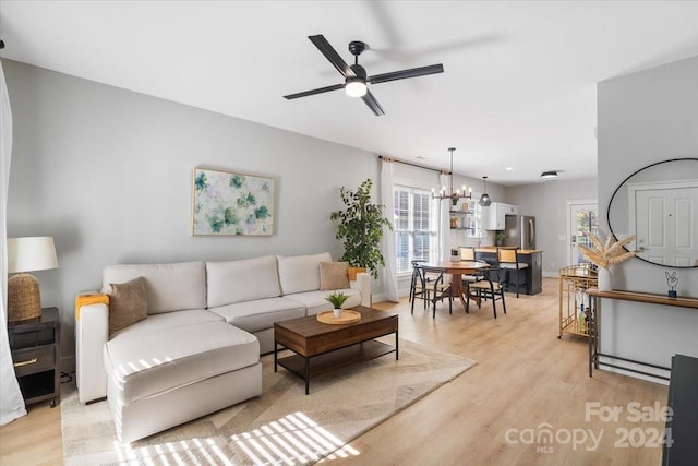 living room with ceiling fan with notable chandelier, light hardwood / wood-style flooring, and a healthy amount of sunlight