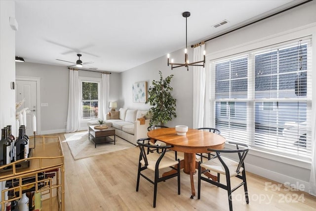 dining room with ceiling fan with notable chandelier and light hardwood / wood-style floors