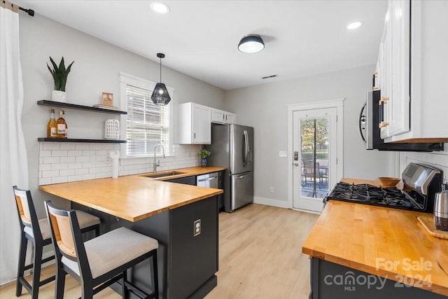 kitchen with stainless steel appliances, sink, decorative light fixtures, white cabinetry, and a breakfast bar area