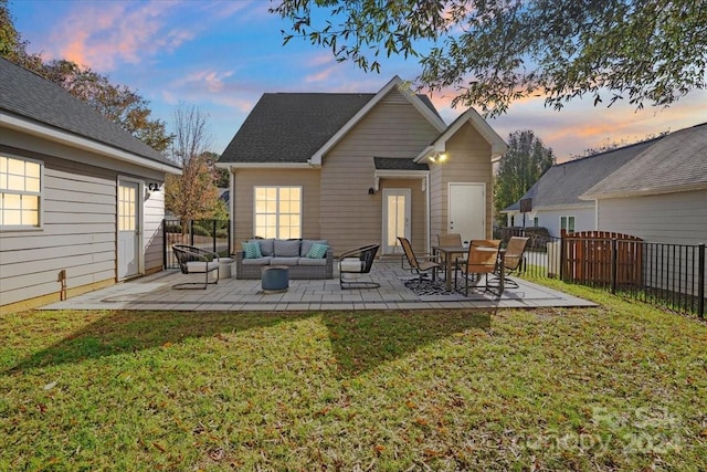 back house at dusk featuring a patio area, outdoor lounge area, and a yard