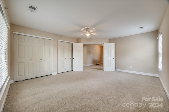 unfurnished bedroom featuring multiple closets, ceiling fan, and light colored carpet