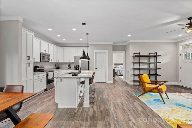 kitchen featuring white cabinets, light stone counters, an island with sink, and appliances with stainless steel finishes