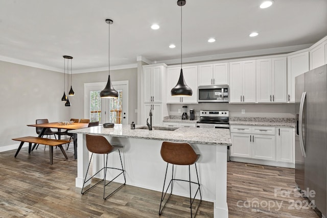 kitchen featuring dark hardwood / wood-style flooring, stainless steel appliances, decorative light fixtures, white cabinetry, and an island with sink