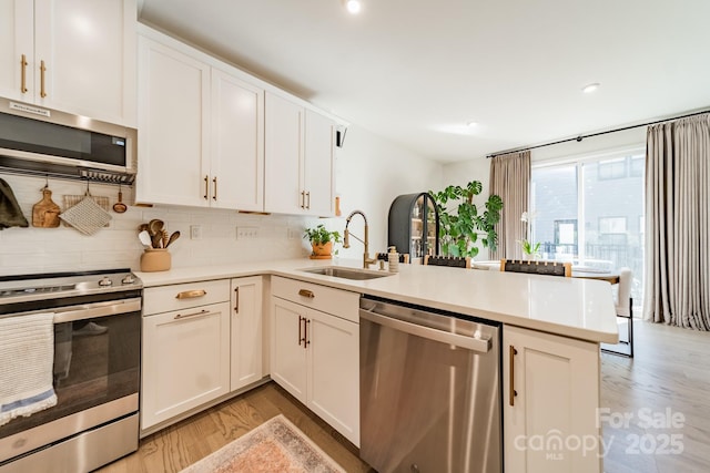 kitchen featuring a peninsula, light countertops, appliances with stainless steel finishes, and a sink