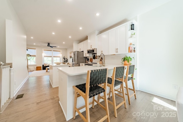 kitchen with light wood-type flooring, white cabinetry, recessed lighting, stainless steel appliances, and a peninsula