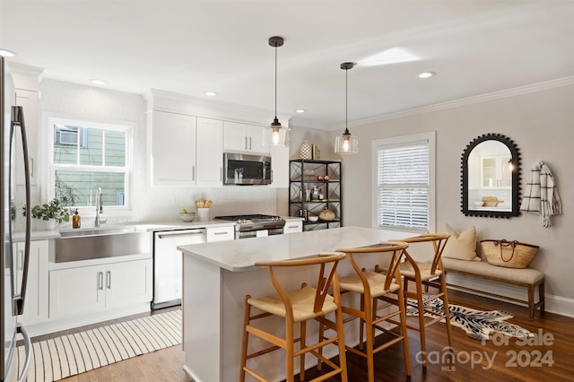 kitchen with appliances with stainless steel finishes, a kitchen island, white cabinetry, and a healthy amount of sunlight