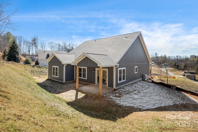 rear view of house with central air condition unit, a shingled roof, a yard, board and batten siding, and a patio area