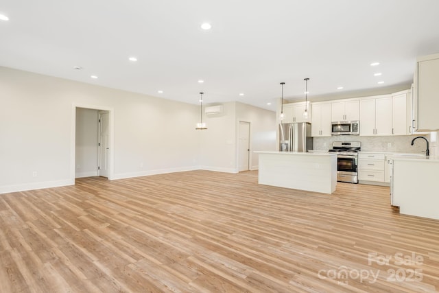 kitchen featuring white cabinets, open floor plan, light countertops, appliances with stainless steel finishes, and hanging light fixtures