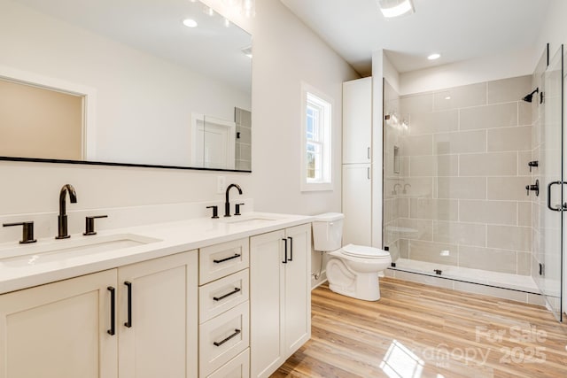 bathroom with double vanity, a stall shower, a sink, and wood finished floors