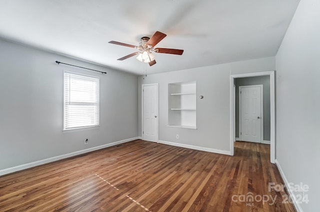 unfurnished room with built in shelves, dark hardwood / wood-style floors, and ceiling fan