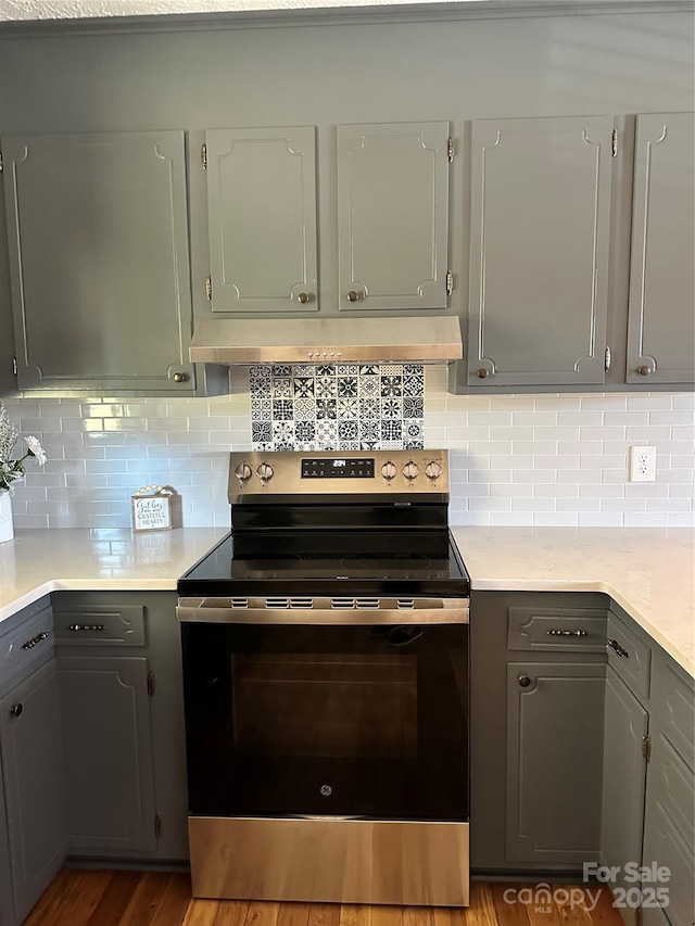 kitchen featuring extractor fan, gray cabinetry, electric stove, hardwood / wood-style floors, and backsplash