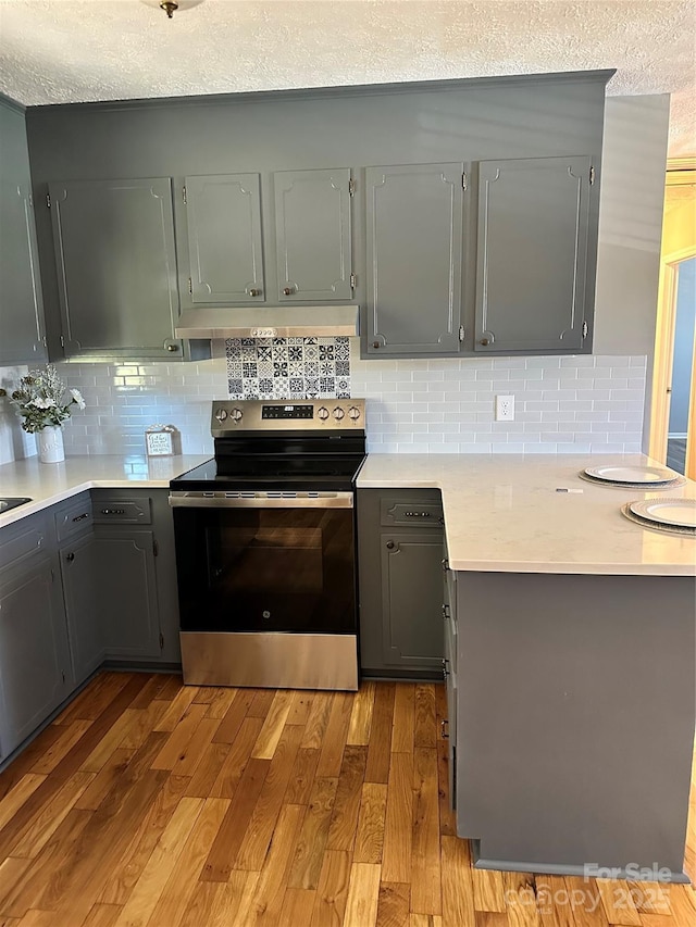 kitchen featuring stainless steel range with electric cooktop, gray cabinetry, a textured ceiling, light hardwood / wood-style floors, and backsplash