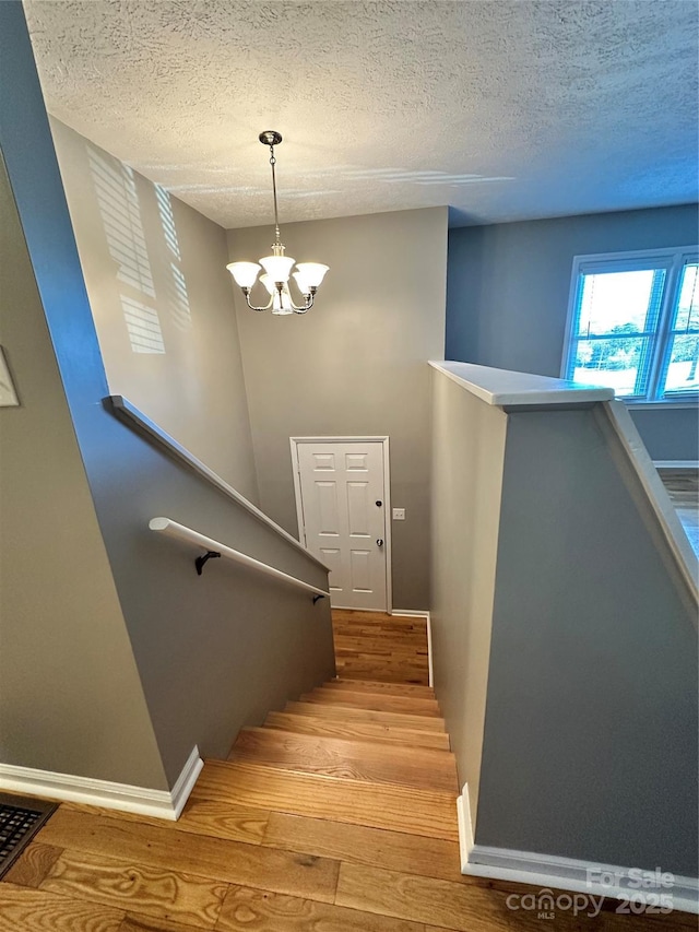 staircase featuring a notable chandelier, hardwood / wood-style flooring, and a textured ceiling