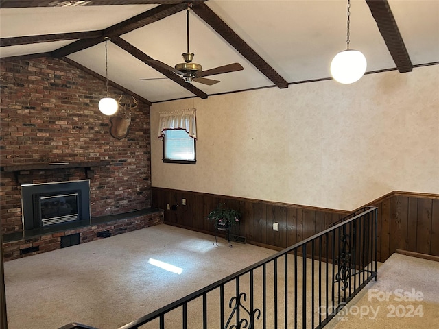 unfurnished living room with vaulted ceiling with beams, carpet flooring, wooden walls, a brick fireplace, and ceiling fan