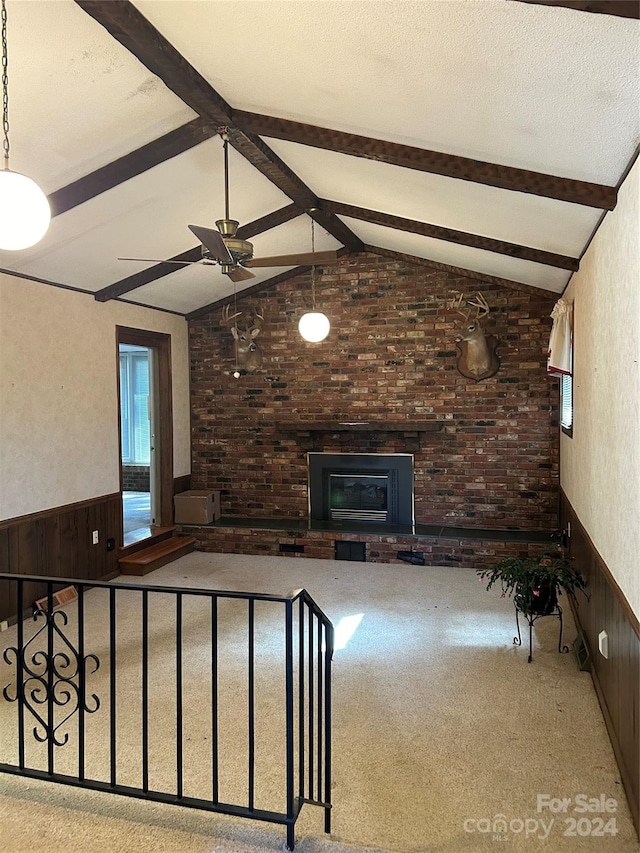 unfurnished living room featuring a fireplace, light carpet, vaulted ceiling with beams, and wooden walls