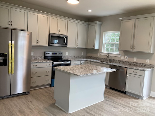 kitchen with appliances with stainless steel finishes, light wood-type flooring, a kitchen island, and sink