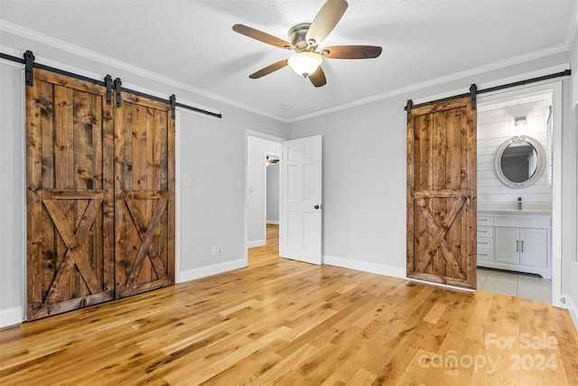 unfurnished bedroom with a barn door, ensuite bathroom, light hardwood / wood-style flooring, and ceiling fan