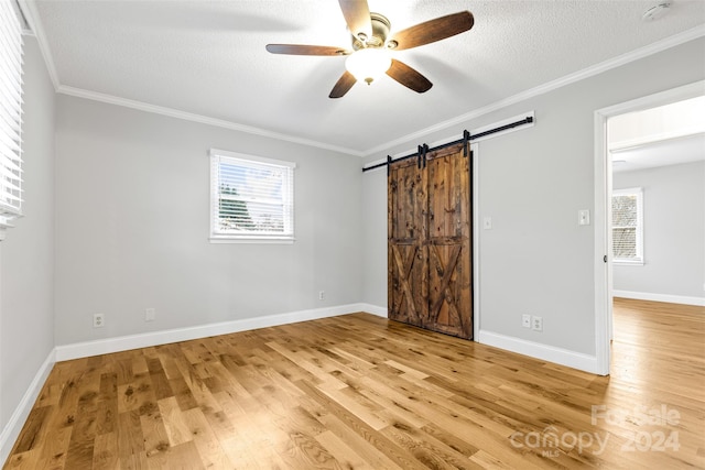 unfurnished bedroom featuring a barn door, ceiling fan, hardwood / wood-style floors, and a textured ceiling