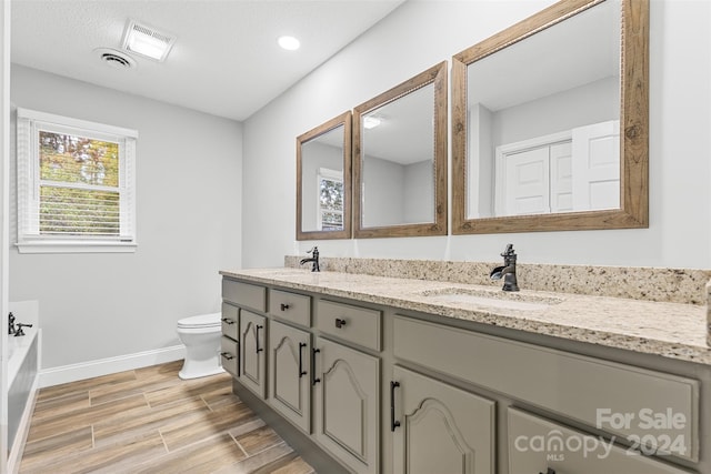 bathroom with a tub to relax in, toilet, vanity, and hardwood / wood-style flooring