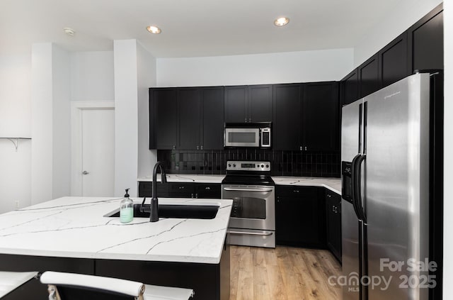 kitchen featuring appliances with stainless steel finishes, sink, backsplash, light stone counters, and a center island with sink