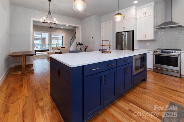 kitchen featuring white cabinetry, wall chimney range hood, decorative light fixtures, and appliances with stainless steel finishes