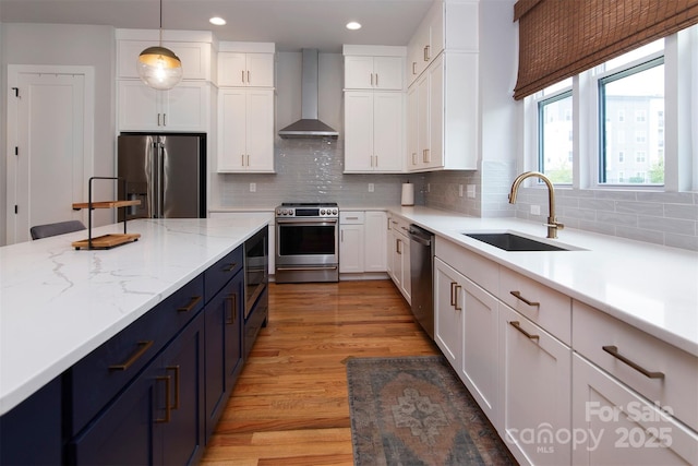 kitchen with sink, stainless steel appliances, white cabinets, decorative light fixtures, and wall chimney exhaust hood