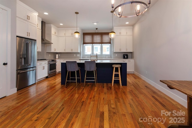 kitchen featuring a center island, hanging light fixtures, wall chimney range hood, stainless steel appliances, and white cabinets