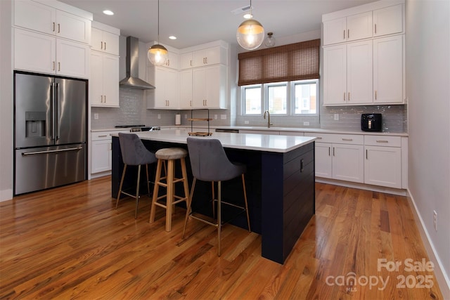 kitchen featuring white cabinetry, wall chimney exhaust hood, high end fridge, and hanging light fixtures