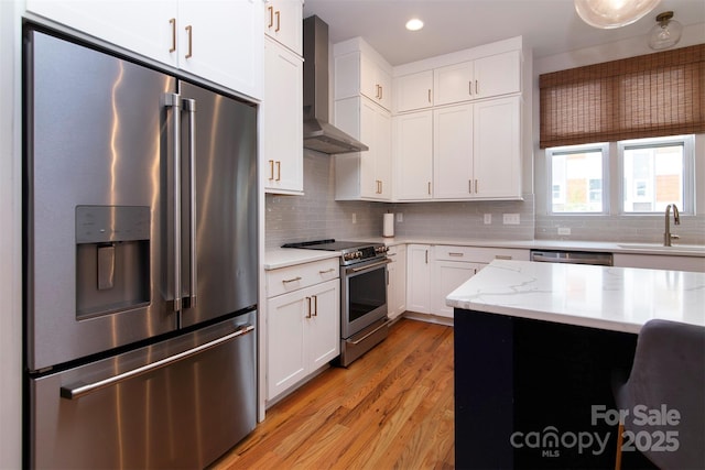 kitchen with wall chimney range hood, sink, appliances with stainless steel finishes, tasteful backsplash, and white cabinets