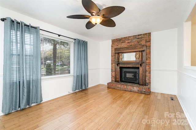 unfurnished living room featuring ceiling fan, a fireplace, a textured ceiling, and light wood-type flooring