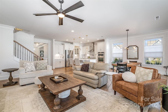 living room featuring crown molding, light hardwood / wood-style flooring, ceiling fan with notable chandelier, and sink