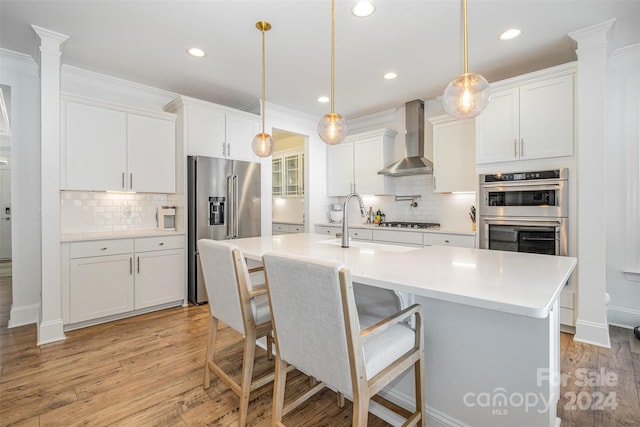 kitchen featuring white cabinetry, hanging light fixtures, light hardwood / wood-style floors, and wall chimney range hood