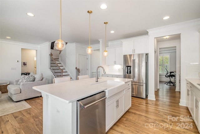 kitchen featuring white cabinets, appliances with stainless steel finishes, a center island with sink, and pendant lighting