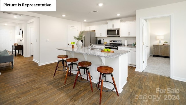 kitchen featuring a center island with sink, appliances with stainless steel finishes, a kitchen bar, dark hardwood / wood-style flooring, and white cabinets