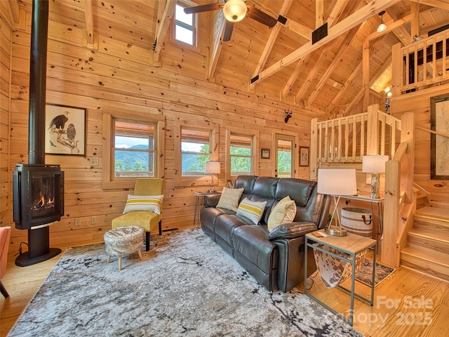 living room with ceiling fan, wooden walls, wooden ceiling, beamed ceiling, and a wood stove