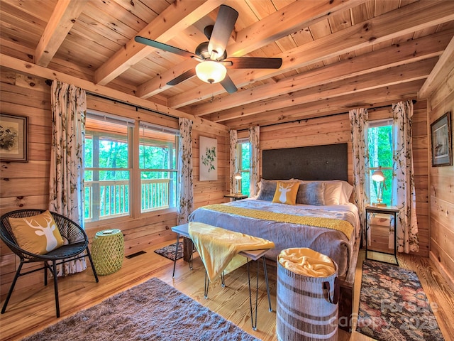 bedroom with multiple windows, beam ceiling, light wood-type flooring, and wood walls