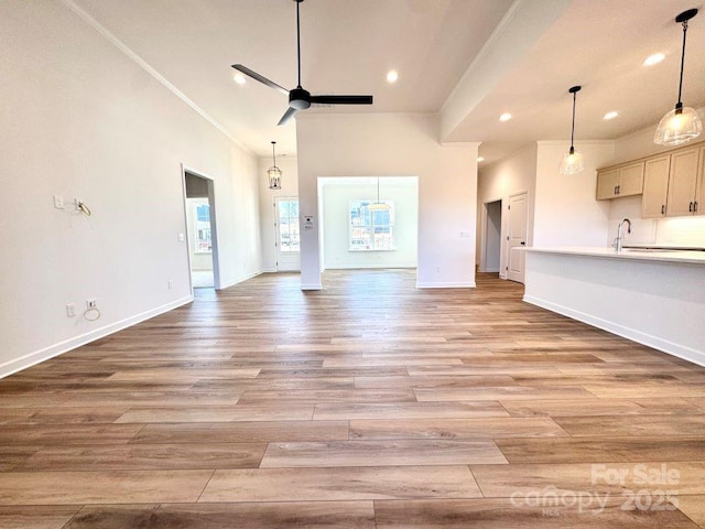 unfurnished living room featuring light hardwood / wood-style flooring, a towering ceiling, crown molding, ceiling fan, and sink