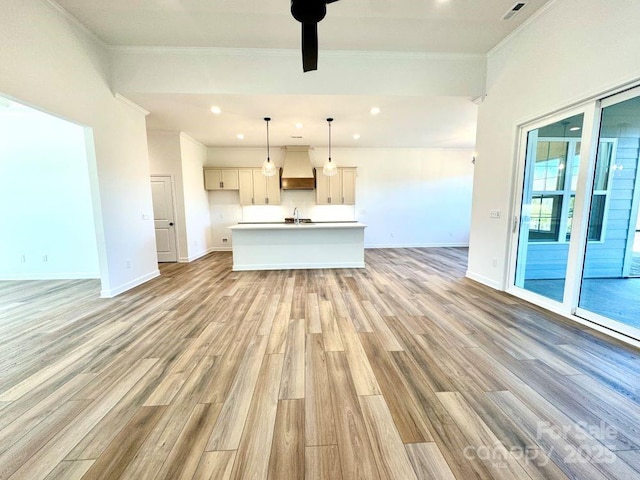 unfurnished living room featuring ceiling fan, light hardwood / wood-style floors, ornamental molding, and sink