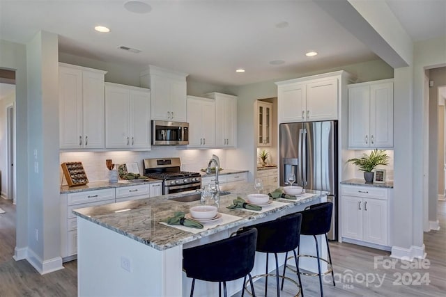 kitchen with a center island with sink, stainless steel appliances, white cabinetry, sink, and a breakfast bar