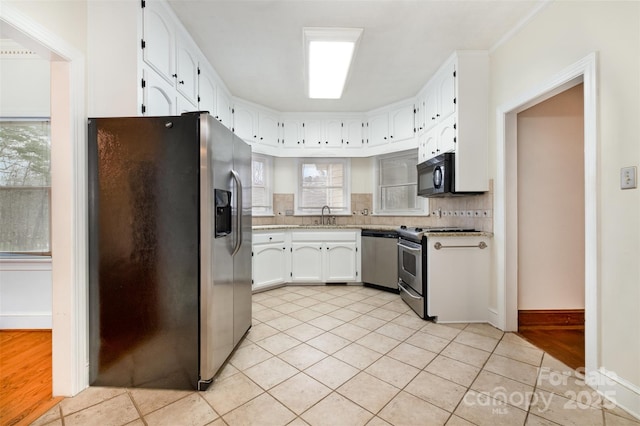 kitchen featuring light tile patterned flooring, a sink, white cabinetry, appliances with stainless steel finishes, and decorative backsplash