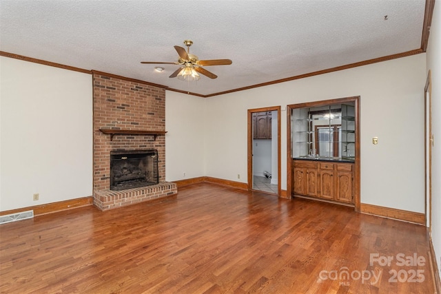 unfurnished living room with a brick fireplace, a textured ceiling, visible vents, and wood finished floors