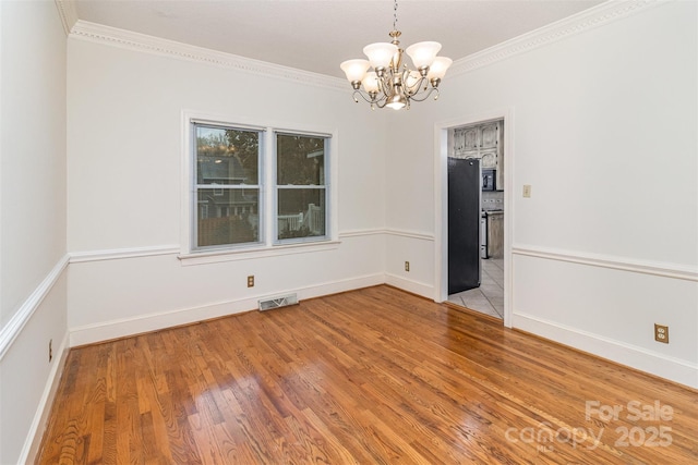 spare room with a chandelier, wood finished floors, visible vents, baseboards, and crown molding