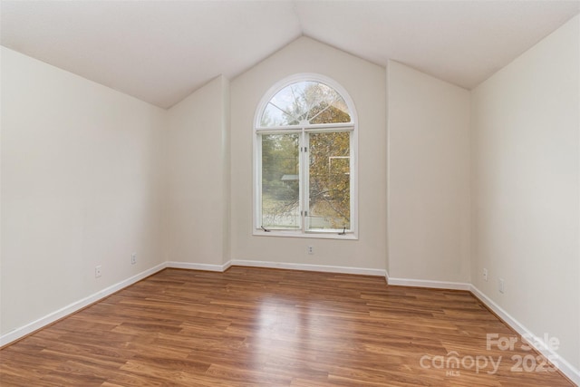 spare room with lofted ceiling, baseboards, and wood finished floors