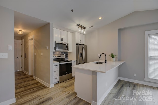 kitchen with stainless steel appliances, light wood-style flooring, white cabinetry, a sink, and a peninsula