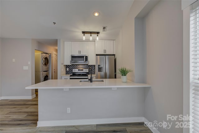 kitchen featuring stacked washer and clothes dryer, appliances with stainless steel finishes, a peninsula, a sink, and backsplash