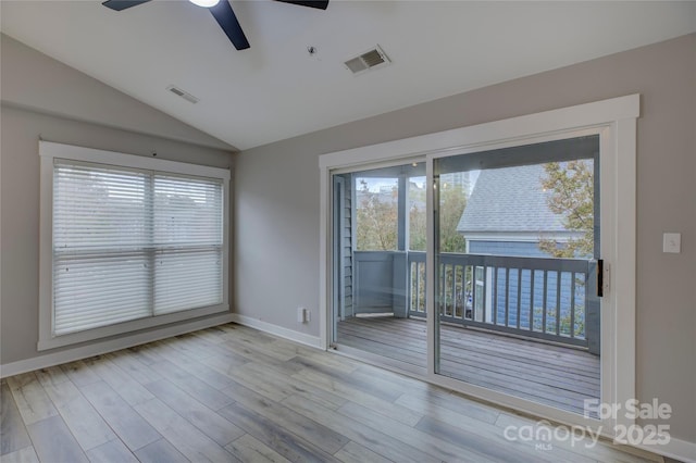 empty room featuring lofted ceiling, visible vents, a wealth of natural light, and wood finished floors