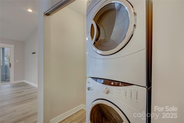 laundry room with light wood-type flooring, stacked washer and dryer, and baseboards